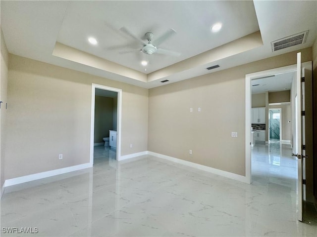 empty room featuring a raised ceiling, visible vents, marble finish floor, and baseboards