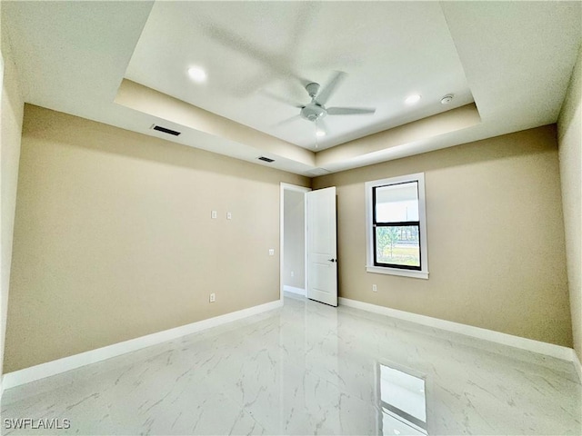 spare room featuring a raised ceiling, marble finish floor, and baseboards