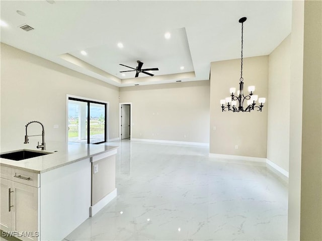 kitchen featuring a tray ceiling, marble finish floor, visible vents, a sink, and baseboards