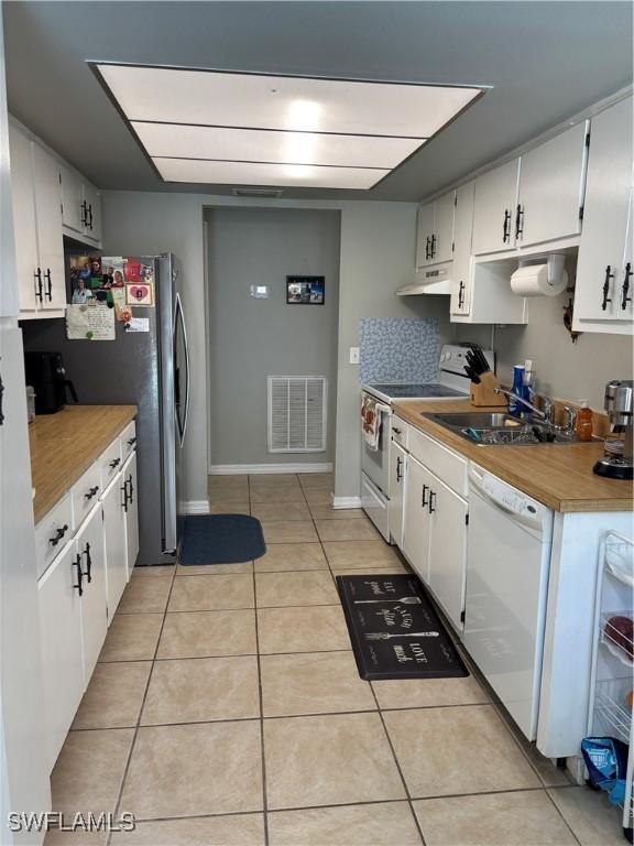 kitchen featuring white appliances, light tile patterned floors, visible vents, under cabinet range hood, and a sink