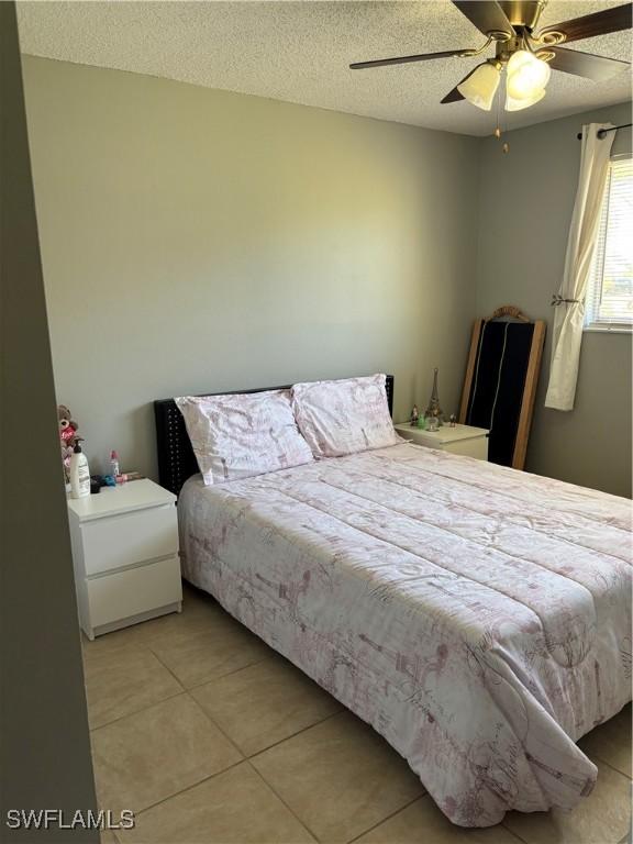 tiled bedroom with ceiling fan and a textured ceiling