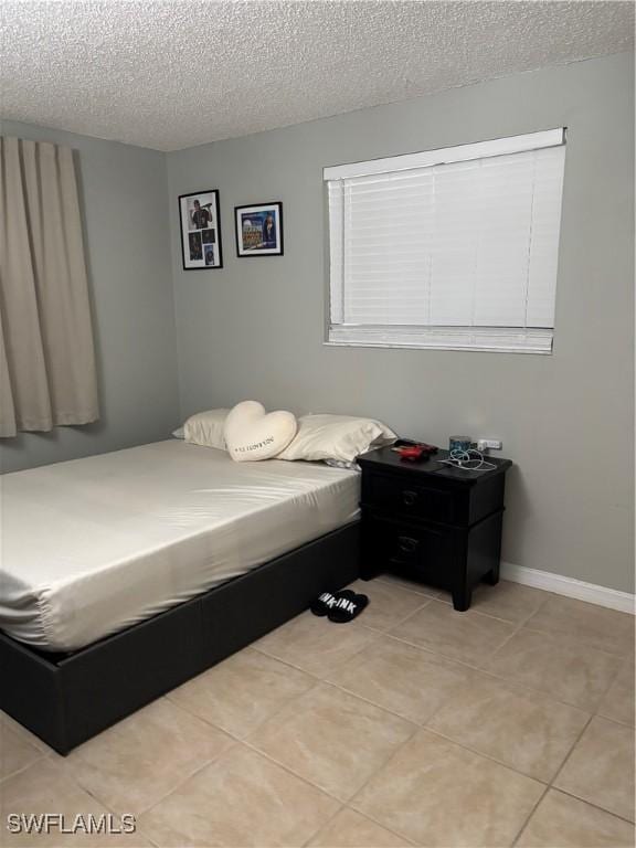 bedroom with a textured ceiling, light tile patterned flooring, and baseboards