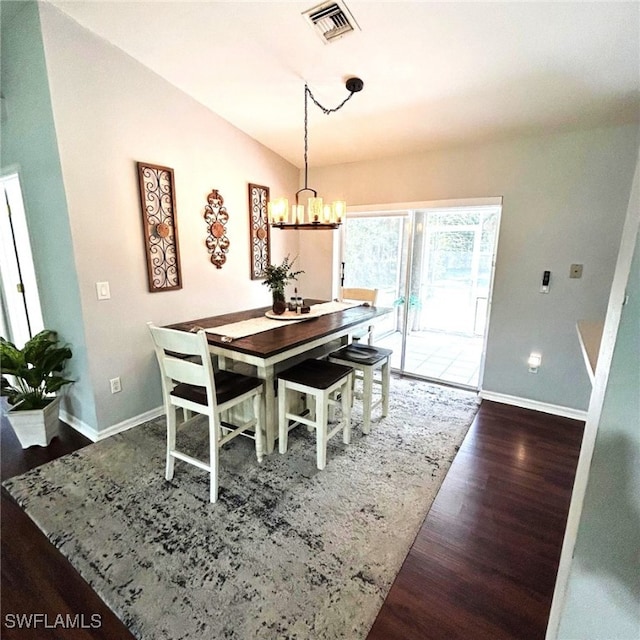 dining room featuring a notable chandelier, visible vents, vaulted ceiling, wood finished floors, and baseboards