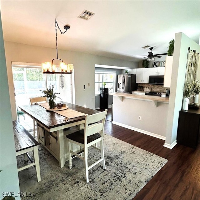 dining area featuring ceiling fan with notable chandelier, dark wood-type flooring, visible vents, and baseboards