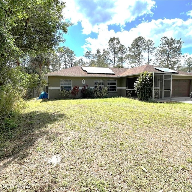 view of front of home with stucco siding, a sunroom, roof mounted solar panels, a garage, and a front lawn