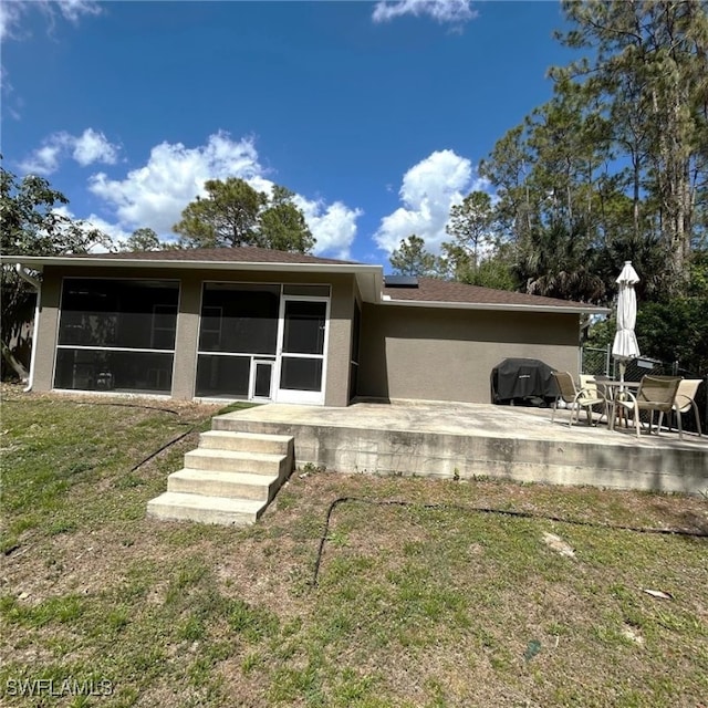 rear view of property with a sunroom, a patio, a lawn, and stucco siding