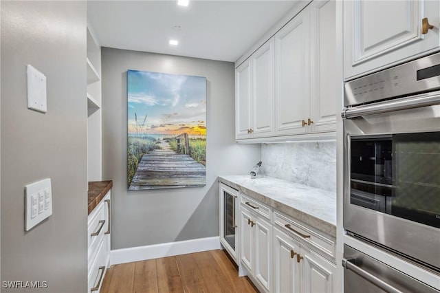 kitchen featuring light wood-style flooring, white cabinets, backsplash, and beverage cooler