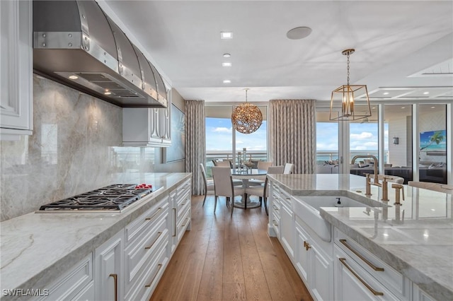 kitchen with under cabinet range hood, white cabinetry, light wood-style floors, backsplash, and stainless steel gas stovetop