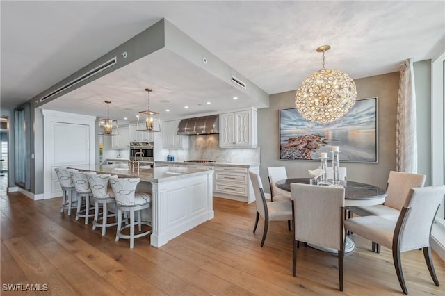 kitchen featuring light wood finished floors, visible vents, an inviting chandelier, wall chimney range hood, and white cabinetry