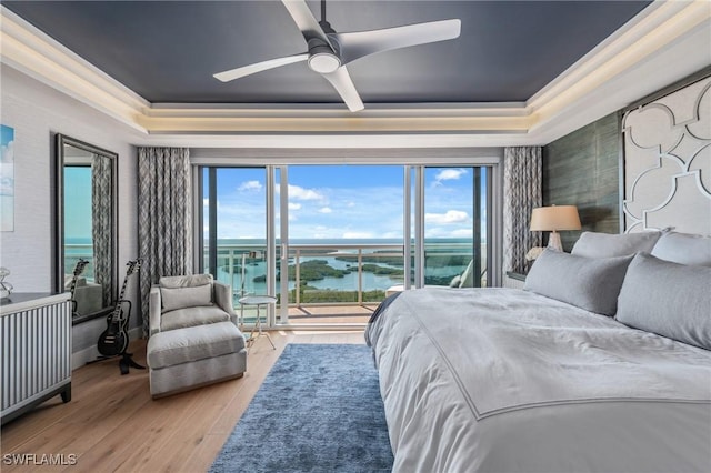 bedroom featuring a water view, access to outside, multiple windows, and a raised ceiling