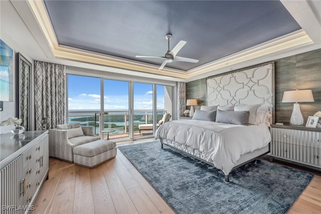 bedroom with access to outside, a ceiling fan, a raised ceiling, and hardwood / wood-style floors