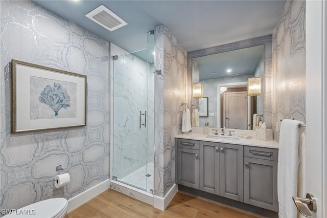 bathroom featuring a marble finish shower, visible vents, toilet, wood finished floors, and vanity