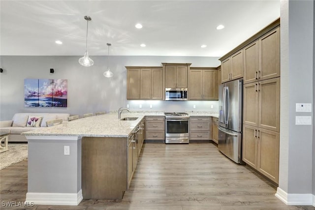 kitchen with light stone counters, appliances with stainless steel finishes, light wood-style floors, and a sink