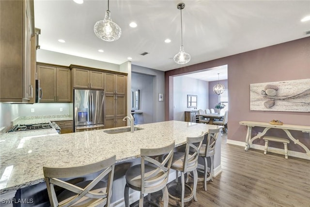 kitchen with light stone countertops, appliances with stainless steel finishes, a peninsula, wood finished floors, and a sink