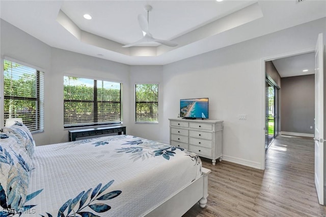 bedroom featuring recessed lighting, a tray ceiling, baseboards, and wood finished floors