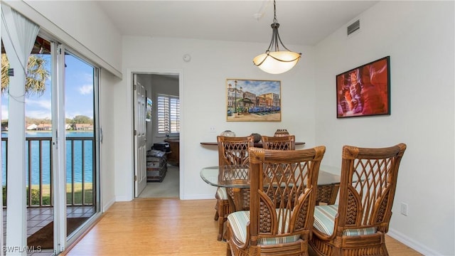 dining room with visible vents, a water view, light wood-style flooring, and baseboards