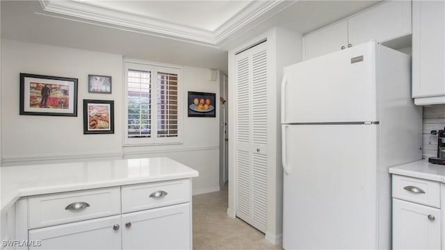 kitchen with light countertops, ornamental molding, freestanding refrigerator, and white cabinetry