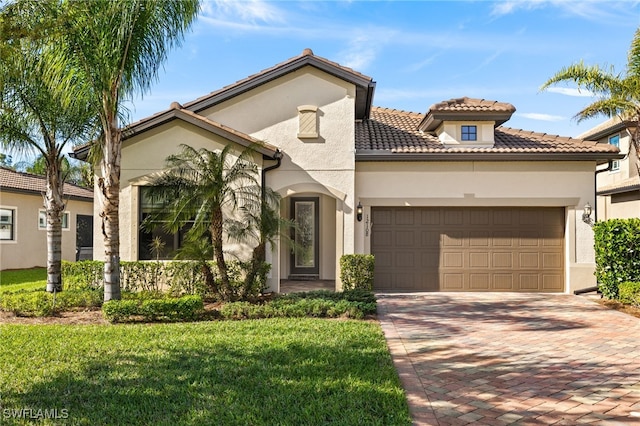 mediterranean / spanish house featuring an attached garage, stucco siding, a front lawn, a tile roof, and decorative driveway