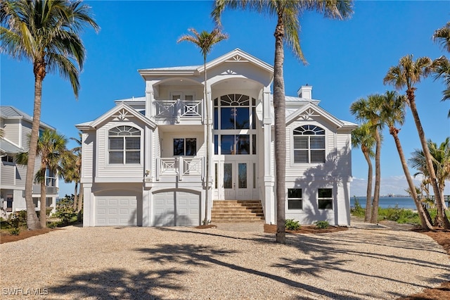 view of front of home with an attached garage, a balcony, driveway, french doors, and a chimney