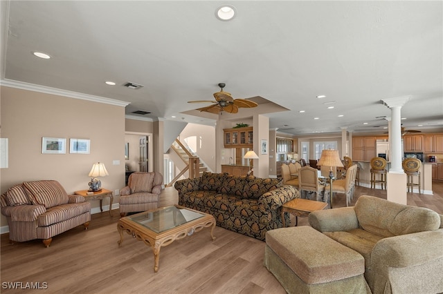 living area featuring stairway, light wood-style flooring, ornamental molding, ceiling fan, and ornate columns