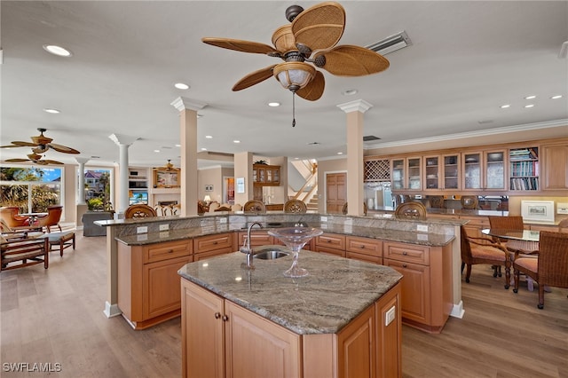 kitchen with crown molding, a large island, light wood-style floors, a sink, and ornate columns