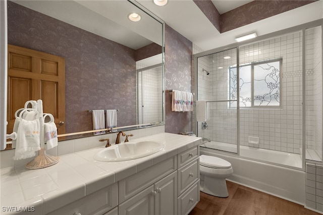 bathroom featuring toilet, wood finished floors, vanity, combined bath / shower with glass door, and wallpapered walls