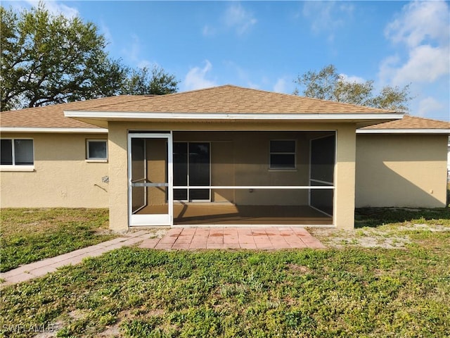 back of property featuring a yard, a shingled roof, a sunroom, and stucco siding