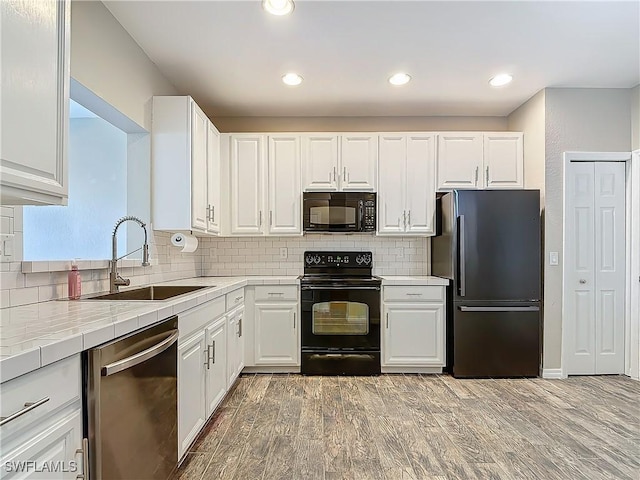 kitchen with tile counters, white cabinets, a sink, black appliances, and backsplash