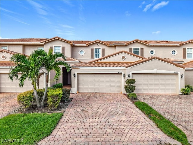 mediterranean / spanish-style home featuring a garage, decorative driveway, a tile roof, and stucco siding