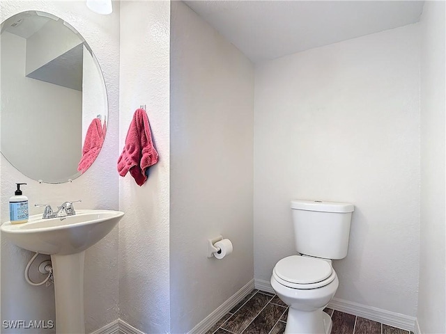 bathroom with wood finish floors, a sink, toilet, and baseboards