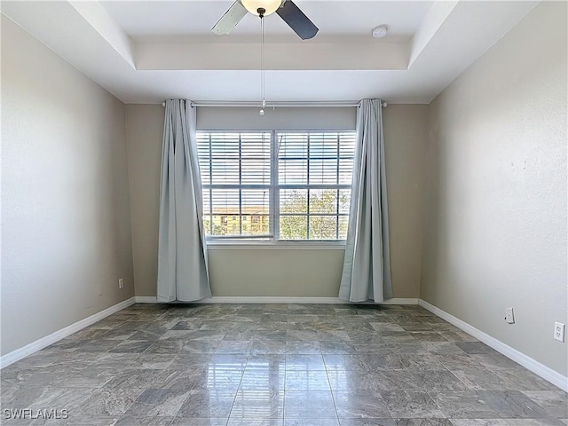 spare room with a ceiling fan, a raised ceiling, and baseboards