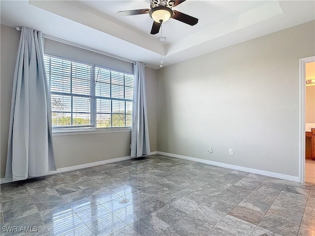 unfurnished room featuring ceiling fan, baseboards, and a raised ceiling