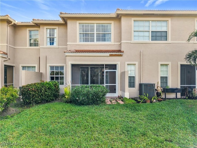 back of property with central air condition unit, a tiled roof, a lawn, and stucco siding