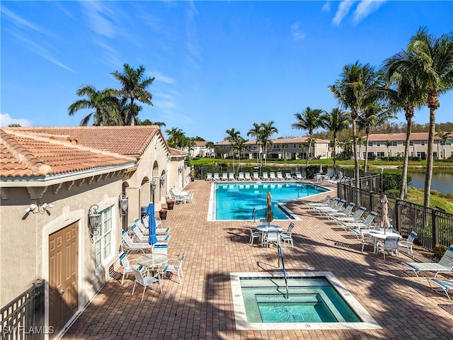 community pool with a patio area, fence, and a hot tub