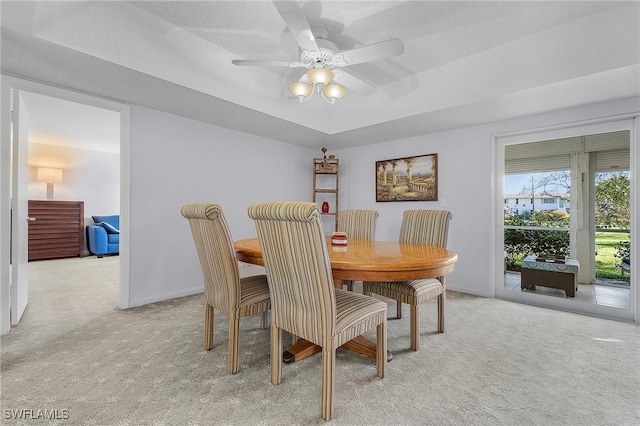 dining room featuring baseboards, ceiling fan, light colored carpet, a textured ceiling, and a raised ceiling