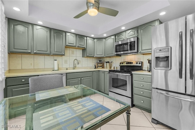 kitchen featuring a sink, backsplash, appliances with stainless steel finishes, green cabinets, and light tile patterned floors