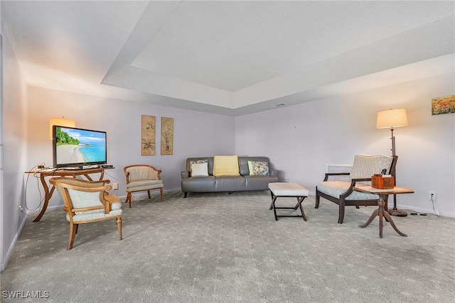 carpeted living area featuring baseboards and a tray ceiling