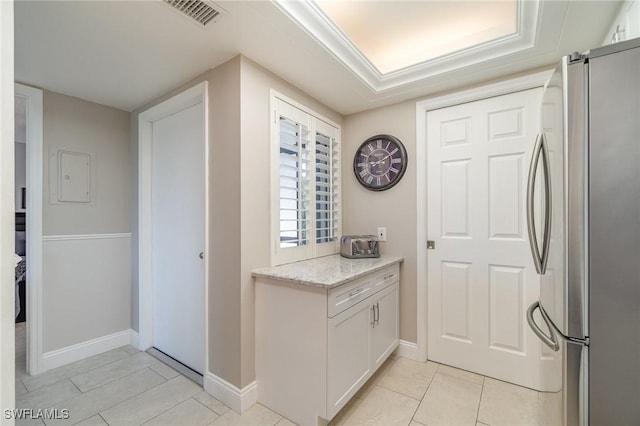 kitchen featuring light tile patterned floors, visible vents, white cabinets, freestanding refrigerator, and light stone countertops