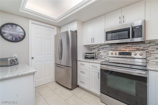 kitchen featuring light tile patterned flooring, white cabinetry, appliances with stainless steel finishes, backsplash, and light stone countertops