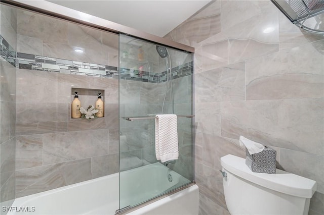 bathroom with combined bath / shower with glass door, toilet, and tile walls