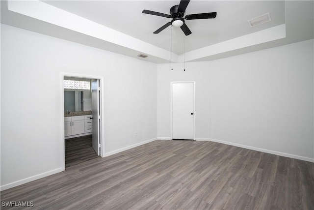 interior space with a tray ceiling, dark wood-style flooring, visible vents, and baseboards