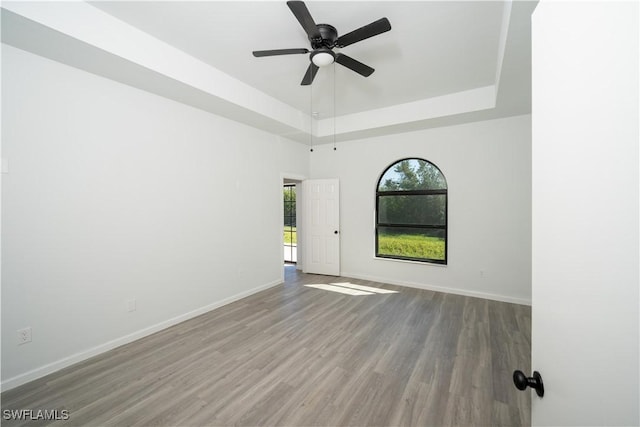 spare room with a ceiling fan, a tray ceiling, baseboards, and wood finished floors