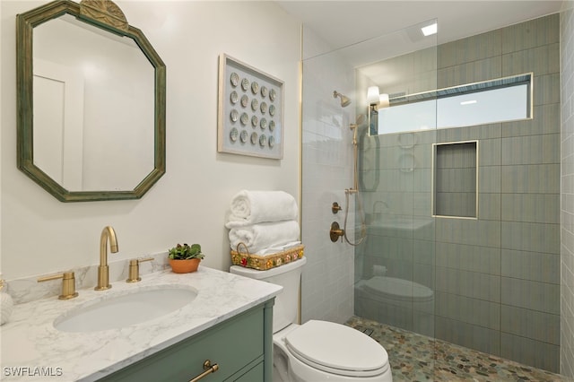 bathroom featuring toilet, tiled shower, and vanity