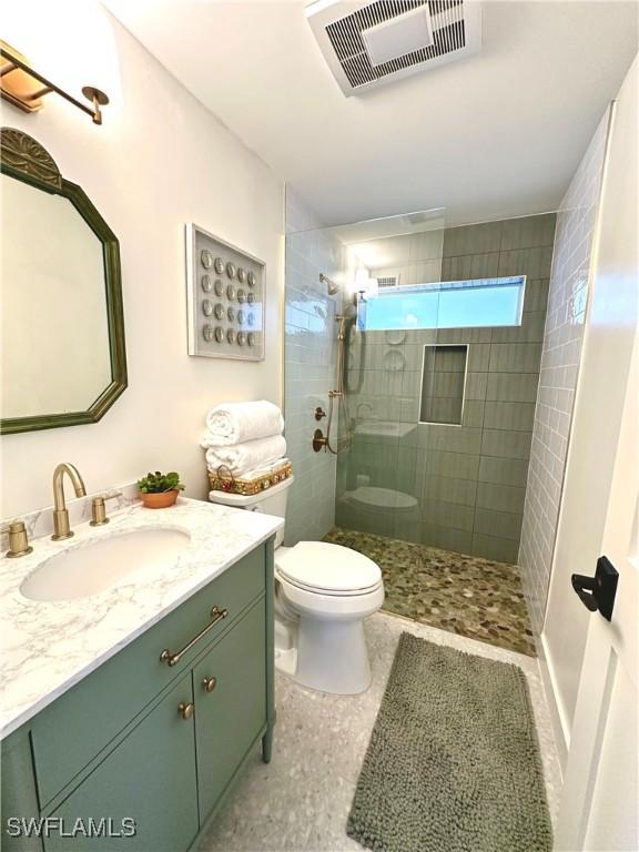 bathroom with toilet, vanity, visible vents, and a tile shower