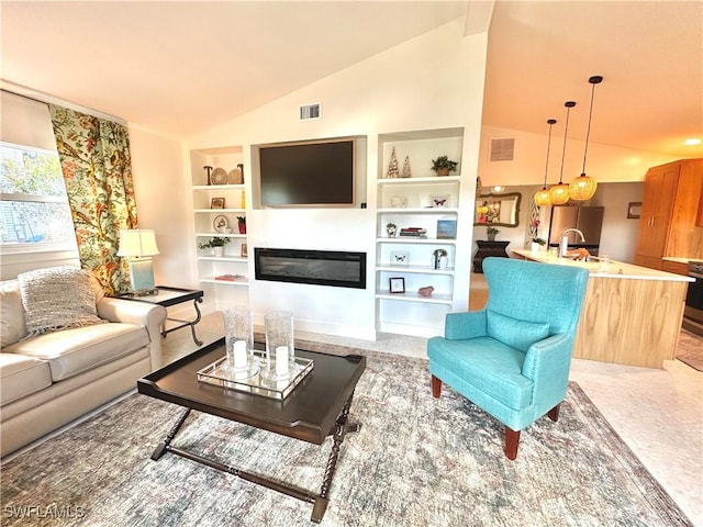 living room featuring vaulted ceiling, a glass covered fireplace, visible vents, and built in features