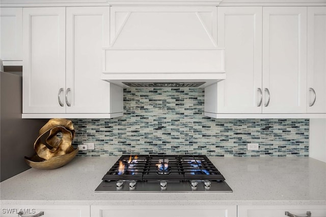 room details featuring backsplash, white cabinets, custom range hood, and stainless steel gas stovetop