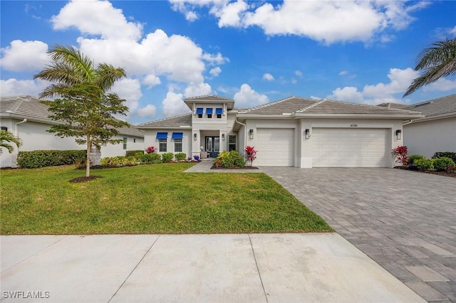 prairie-style house featuring a front lawn, a tiled roof, stucco siding, decorative driveway, and an attached garage