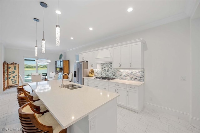 kitchen featuring premium range hood, a center island with sink, decorative backsplash, appliances with stainless steel finishes, and a sink