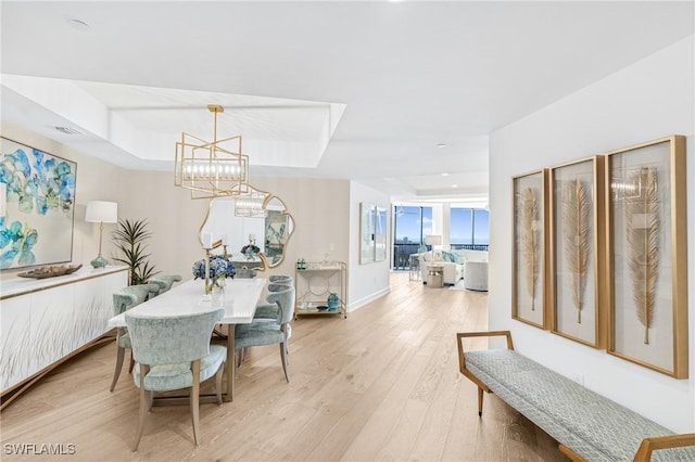 dining room featuring light wood-style floors, a tray ceiling, baseboards, and an inviting chandelier