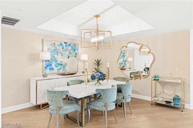 dining area with a tray ceiling, wood finished floors, visible vents, and baseboards